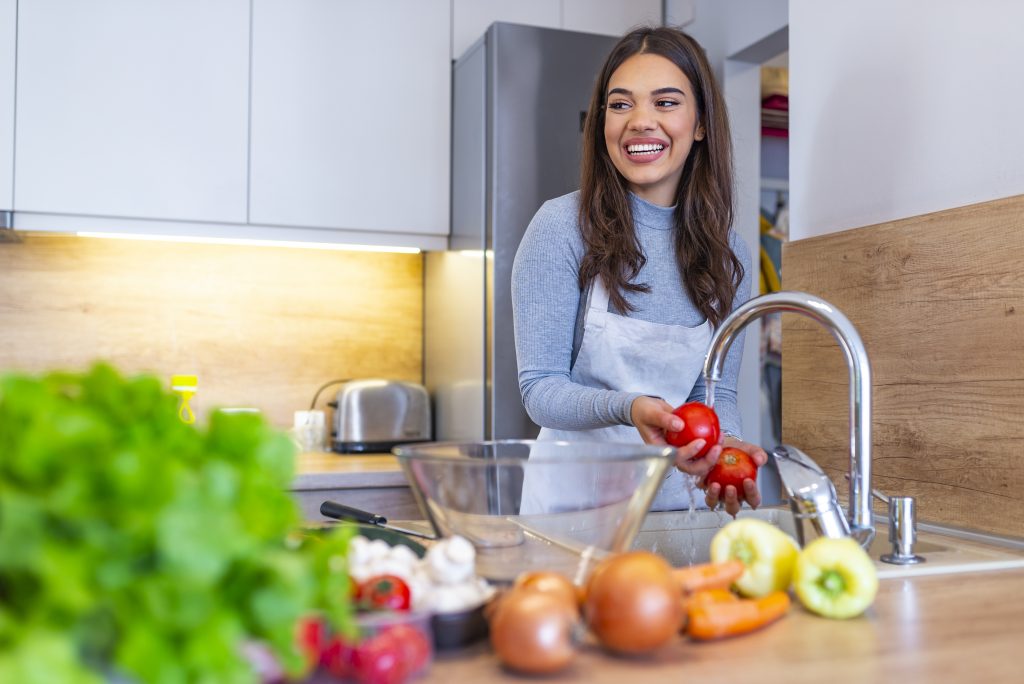 Young woman washes the vegetables in domestic kitchen