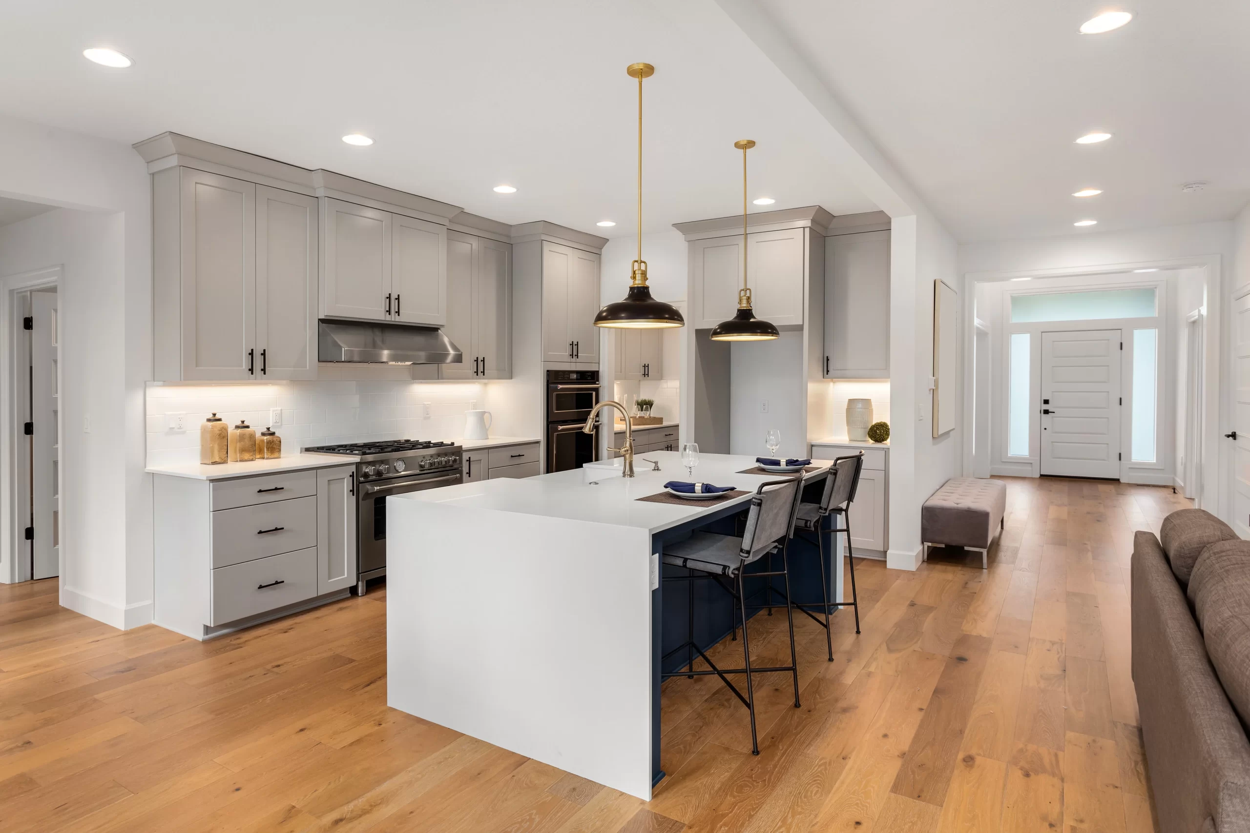Bright modern kitchen with gray cabinets, a large white island, pendant lights, and hardwood floors.